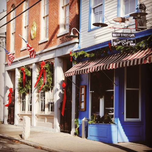 Charming street scene featuring festive decorations, wreaths, and a café with a sign for seafood and oysters.