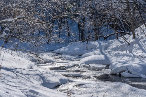 A serene winter scene featuring a snow-covered river surrounded by trees and glistening ice.