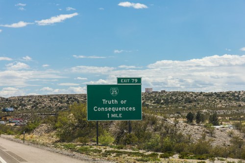 Green highway sign indicating "Truth or Consequences" exit, 1 mile ahead, with a clear blue sky in the background.