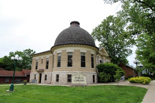 Historic public library building with a dome, surrounded by greenery and a pathway.