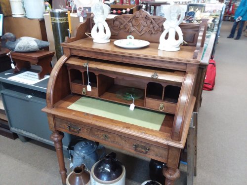 Antique wooden roll-top desk with decorative carvings, open compartments, and a green writing surface.