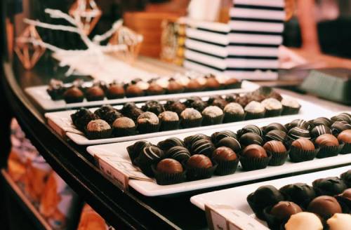 A display of assorted chocolates on white platters, featuring various shapes and toppings, in a cozy setting.