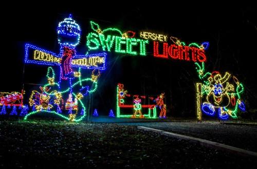 Colorful holiday lights display featuring "Hershey Sweet Lights" with festive characters and decorations at night.