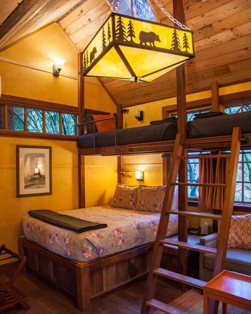 Cozy cabin interior with a lofted bed, floral bedding, wooden accents, and a unique bear-themed light fixture.