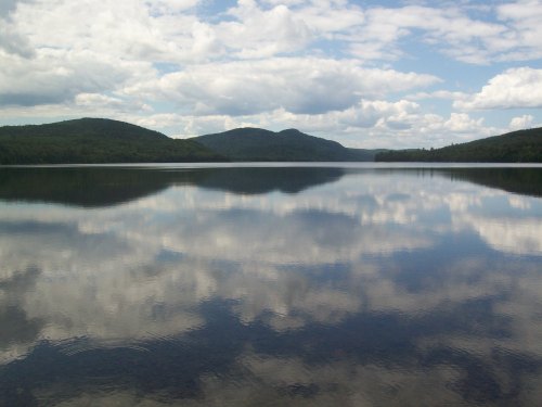 A serene lake reflecting fluffy clouds and green hills under a blue sky.