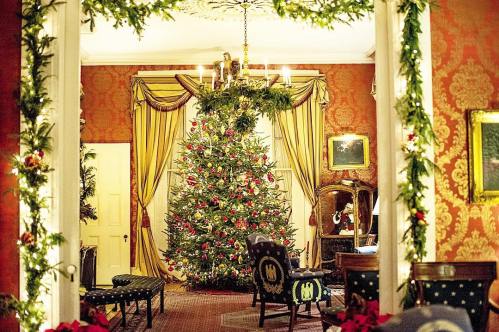 A beautifully decorated room featuring a large Christmas tree, festive garlands, and elegant furnishings.