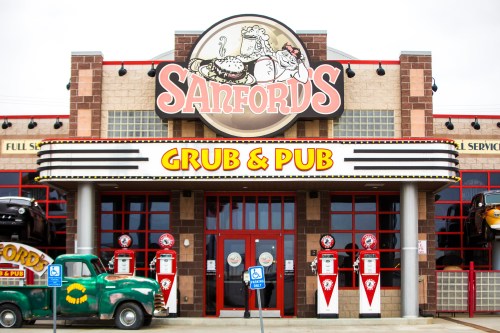 Exterior of Sanford's Grub & Pub, featuring a retro-style sign and vintage cars in front.