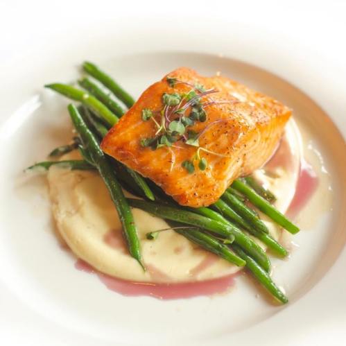 A beautifully plated dish featuring salmon on a bed of creamy sauce, topped with green beans and microgreens.
