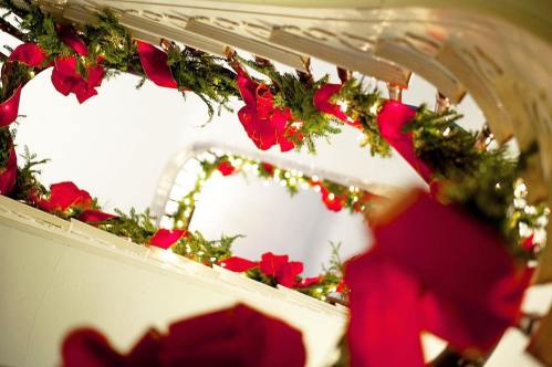 A spiral staircase decorated with greenery and red bows, illuminated by soft lights.