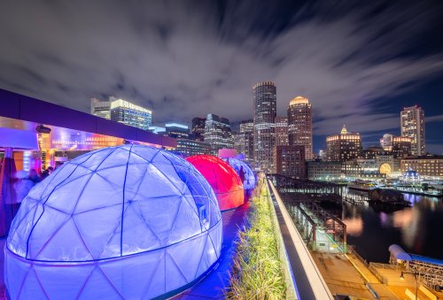 Colorful illuminated domes on a rooftop with a city skyline and water view at night.