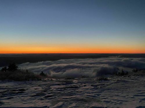 A serene sunset over a snowy landscape, with clouds rolling in below a clear sky.