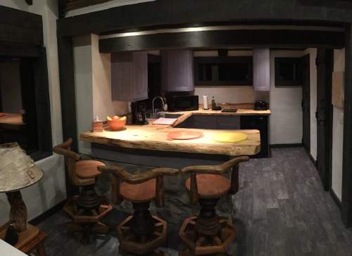 A modern kitchen with wooden accents, featuring a large countertop, bar stools, and dark cabinetry.