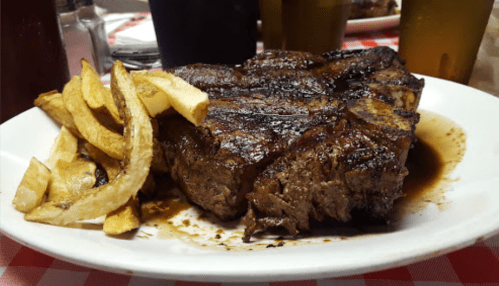 A plate of grilled steak with a side of golden fries, served on a checkered tablecloth.