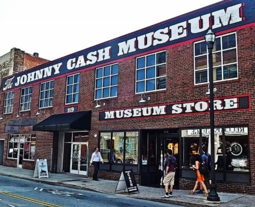 Exterior of the Johnny Cash Museum, featuring a red sign and a museum store entrance, with people walking by.