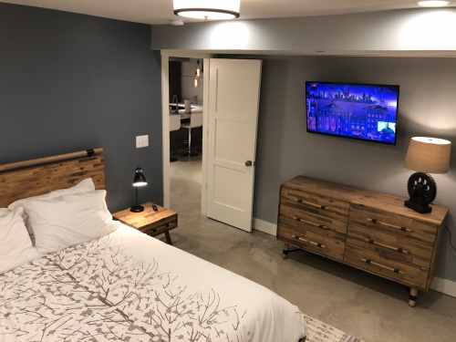 Cozy bedroom with a wooden bed, nightstand, dresser, and a wall-mounted TV in a modern, softly lit space.