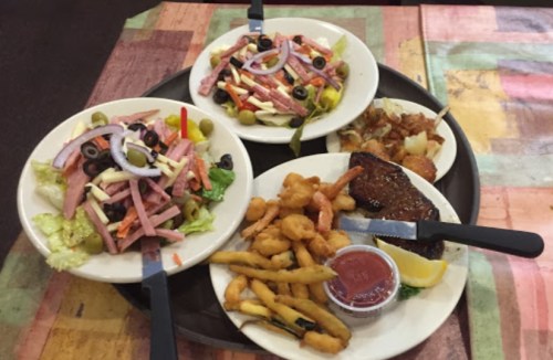 Three plates of food on a tray: salads with ham and olives, a steak, and fried shrimp with dipping sauce.