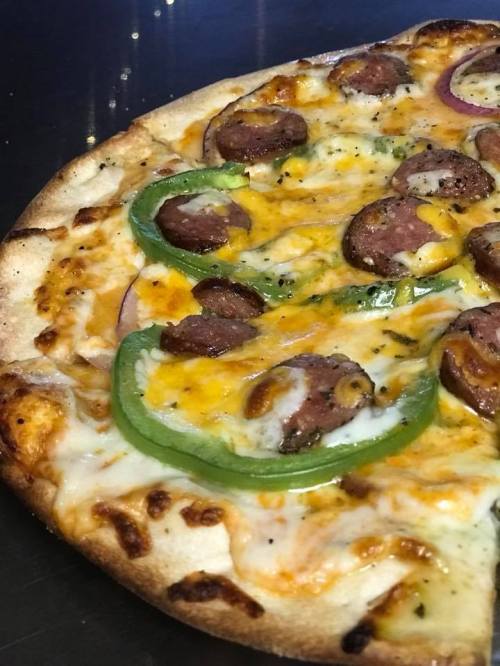 A close-up of a pizza topped with cheese, green peppers, red onions, and slices of sausage on a golden crust.
