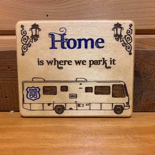 Wooden plaque with the text "Home is where we park it" and an illustration of an RV, featuring a Route 66 sign.