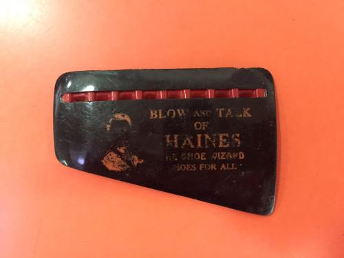 A vintage shoehorn with the text "Blow Ant Talk of Haines, The Shoe Wizard, Shoes for All" on an orange background.