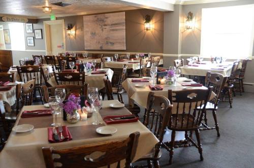 A cozy restaurant interior with wooden tables, chairs, and floral centerpieces, set for dining.
