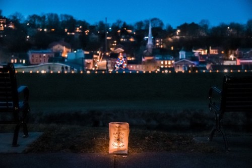 A serene evening view of a town lit up with holiday lights, featuring a glowing lantern in the foreground.