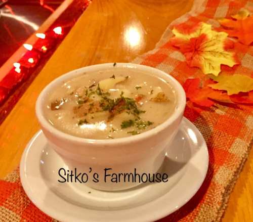 A bowl of creamy soup garnished with herbs, placed on a rustic table with autumn leaves and a warm ambiance.