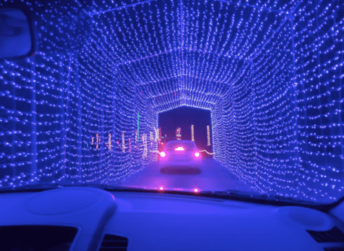 A car drives through a vibrant tunnel of purple and blue lights, creating a festive atmosphere.