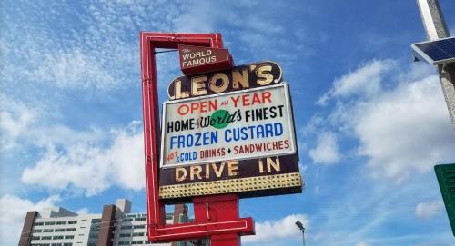 A retro sign for Leon's, advertising frozen custard, cold drinks, and sandwiches, under a blue sky with clouds.