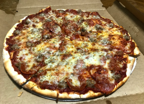 A freshly baked pizza with pepperoni, sausage, and melted cheese, served in a pizza box.