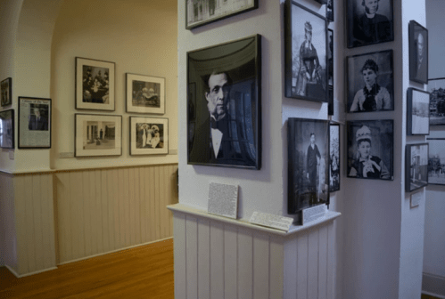 A gallery with black-and-white portraits on the walls and a wooden floor, showcasing historical photographs.