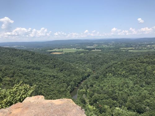 A panoramic view of lush green hills and a winding river under a clear blue sky with scattered clouds.