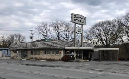 A roadside restaurant with a sign reading "Beacon 443 Restaurant," surrounded by trees and cloudy skies.