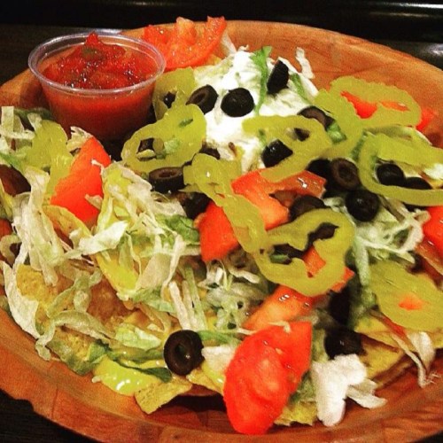 A plate of nachos topped with lettuce, tomatoes, black olives, jalapeños, and a side of salsa.
