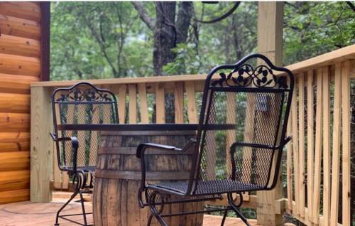 Two metal chairs beside a wooden barrel table on a deck surrounded by trees.