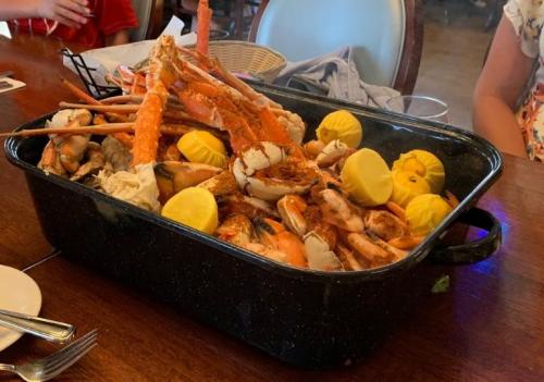 A large black pot filled with seafood, including crabs, shrimp, and lemon wedges, on a wooden table.