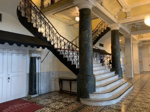 Elegant interior featuring a grand staircase with ornate railings, marble columns, and decorative tiled flooring.