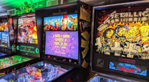 A colorful arcade with pinball machines, featuring "Attack from Mars," "Metallica," and a game in progress.