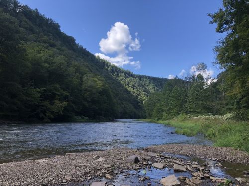 A serene river flows through a lush green valley under a blue sky with fluffy clouds.