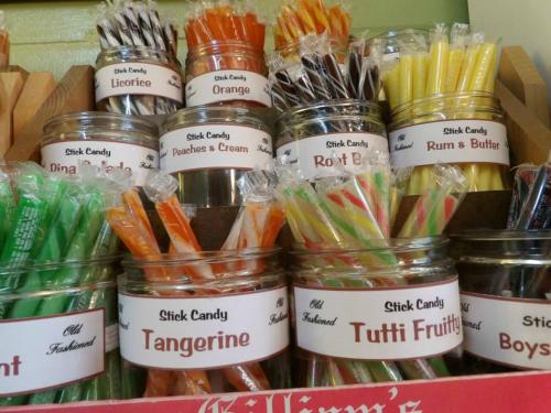 A display of colorful stick candies in jars, labeled with flavors like licorice, orange, and tutti frutti.