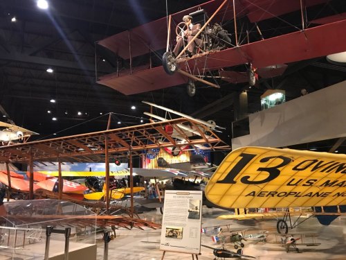 A museum display featuring various vintage aircraft, including a biplane and a replica of an early flying machine.