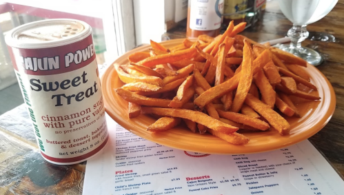 A plate of golden sweet potato fries next to a can of Cajun Power Sweet Treat seasoning.