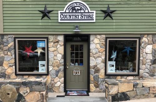 A rustic country store with a stone facade, green siding, and a welcoming entrance featuring star decorations.