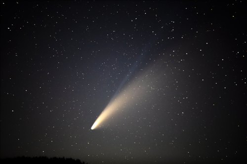 A bright comet with a long tail glides through a starry night sky.