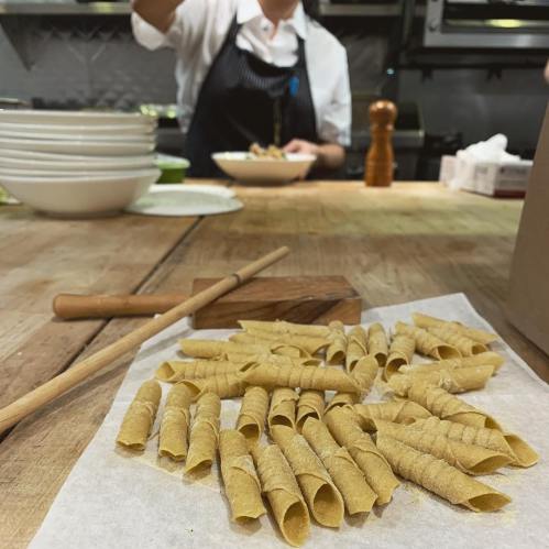 A wooden table with freshly made pasta shapes and a chef preparing a dish in the background.