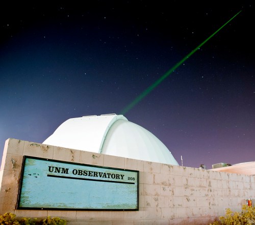 A dome-shaped observatory with a green laser beam pointing into the night sky, surrounded by stars.