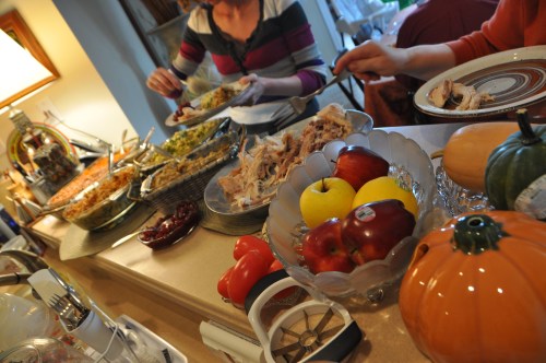 A festive table spread with various dishes, including turkey, sides, and fresh fruit, during a gathering.