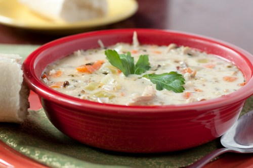 A bowl of creamy chicken soup with vegetables, garnished with parsley, next to a piece of bread on a green napkin.