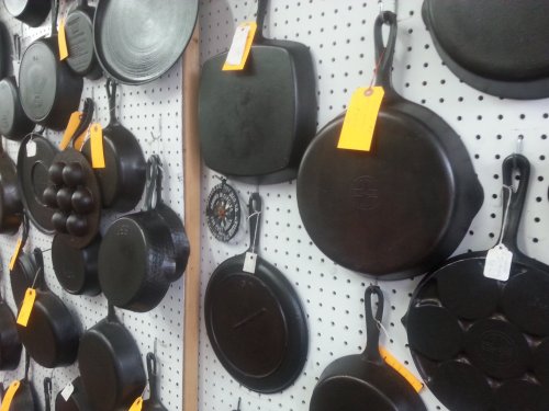 A display of various cast iron pans hanging on a pegboard, each labeled with price tags.