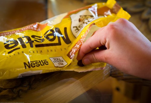 A hand reaching into an open bag of Nestlé Toll House chocolate chips on a wooden table.