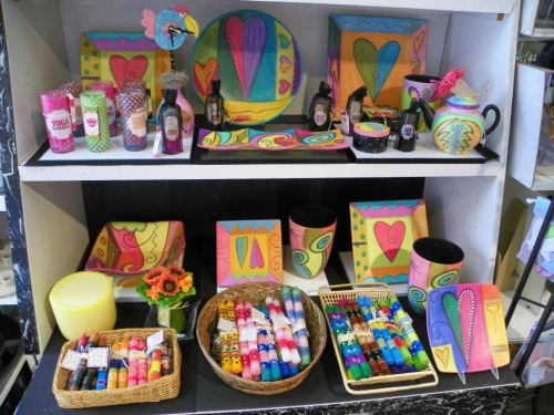 Colorful display of painted items, including plates, bottles, and candles, arranged on shelves with vibrant designs.